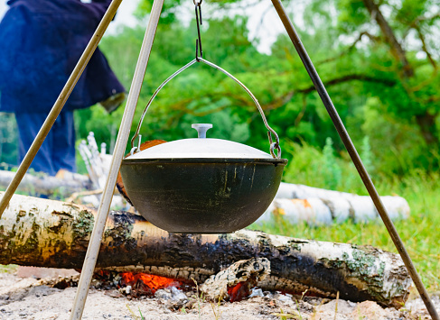 camping cook-kettle hanging on a tripod over a campfire on nature background of green grass