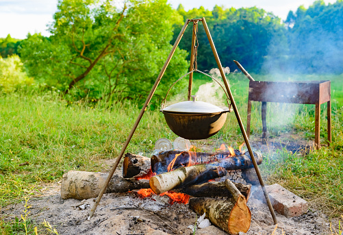 camping cook-kettle hanging on a tripod over a campfire on nature background of green grass