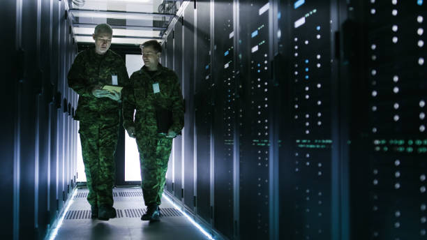 dos hombres militares caminando en el pasillo del centro de datos. uno utiliza la computadora de la tableta, tienen discusión. filas de servidores de datos trabajando por sus lados. - servicio federal de protección fotografías e imágenes de stock