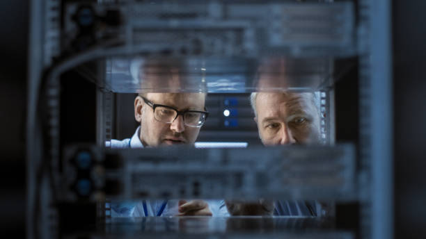 two server engineers install hardware in server rack. they work in big modern data center. - network server rack data center in a row imagens e fotografias de stock