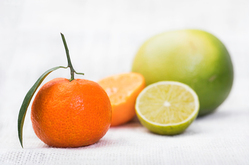 Collection of citrus fruits. A organic tangerine with a leaf and plan stem, a half  mandarin, a half lime and a whole green pomelo oroblanco arranged on a white tablecloth background.