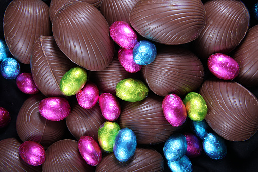 Pile of foil wrapped & unwrapped chocolate easter eggs in pink, blue & lime green.