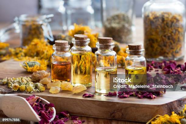 Bottles Of Essential Oil With Dried Rose Petals Chamomile Calendula And Frankincense Stock Photo - Download Image Now