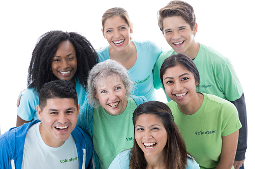 This is a photo of a group of  cheerful medical volunteers as they crowd together and smile at the camera.  The group is diverse both generationally and ethnically.