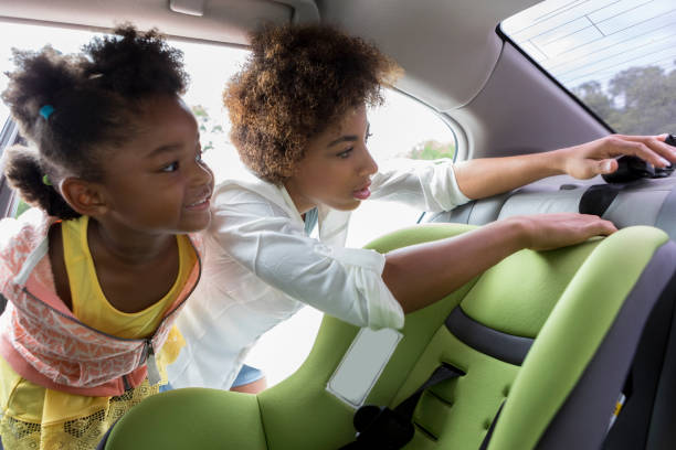 Little girl watches mother install car seat A smiling little girl ducks inside the back seat of her car to watch her serious mother as she tries to anchor a new car seat to the vehicle. latch photos stock pictures, royalty-free photos & images