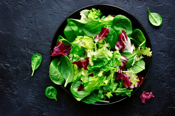 mescolare le foglie di insalata in una ciotola nera - lattuga foto e immagini stock