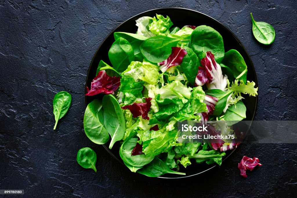 Mix salad leaves in a black bowl Mix salad leaves in a black bowl over dark slate, stone or concrete background.Top view with copy space. Salad Stock Photo