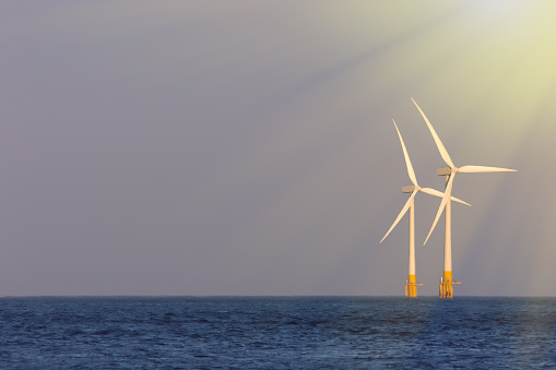 Sustainable resources. Soft seascape with offshore wind turbines illuminated by bright sunshine. Wind, sea and solar power renewable energy represented by windfarm in sun rays in the ocean.