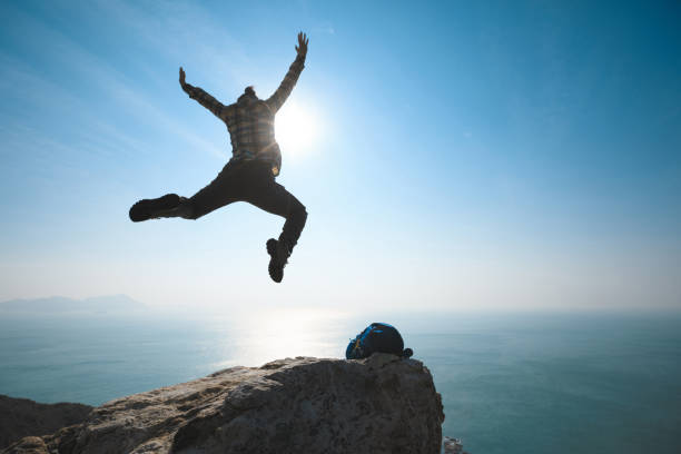istock female hiker jumping on sunrise seaside cliff edge 899832404
