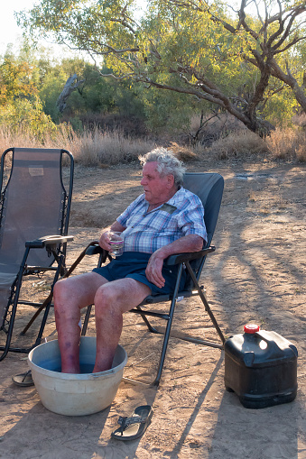 Senior man relaxing with feet in bowl of water in Outback Queensland, Australia