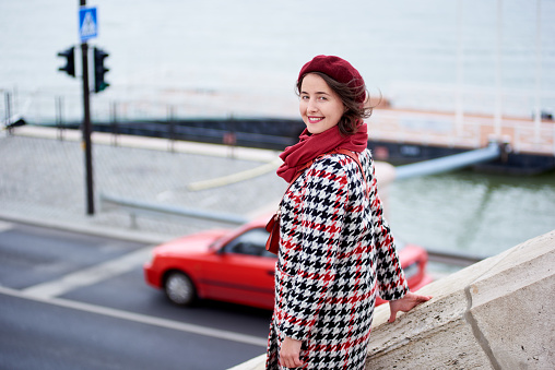 Close-up of a girl descends the steps looking back at the camera. The girl is dressed in a coat, beret and a scarf of one red tone. Below you can see the road. Blurred background