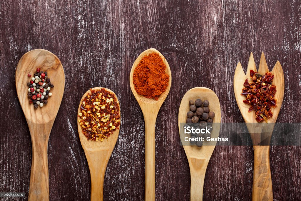 Various spices in wooden spoons on dark brown background. Different types of paprika and peppercorn. Top view. Paprika Stock Photo