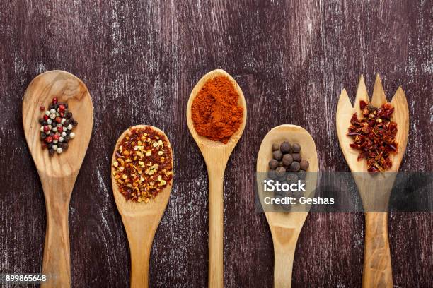 Various Spices In Wooden Spoons On Dark Brown Background Different Types Of Paprika And Peppercorn Top View Stock Photo - Download Image Now