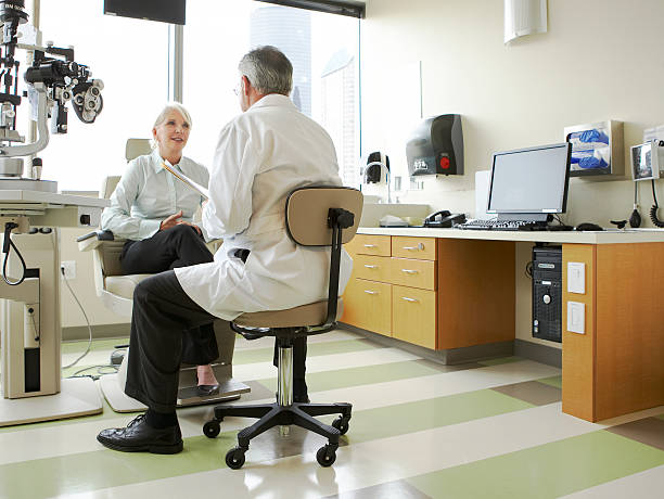 a doctor and patient meet and discuss her vision An opthamologist is listening to the patient in an exam room. eye care professional stock pictures, royalty-free photos & images