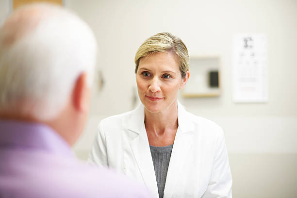 Female Doctor in conversation with mature patient Female opthamologist listening to a patient in an exam room over the shoulder view photos stock pictures, royalty-free photos & images