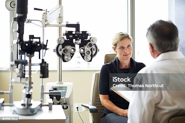 A Woman Listens To Her Opthamologist Stock Photo - Download Image Now - Optometrist, Eye Exam, Discussion
