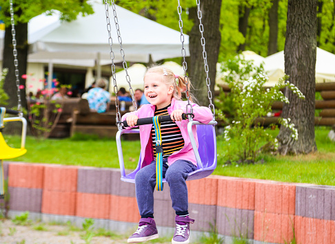 A cute young girl riding a chain carousel swing.