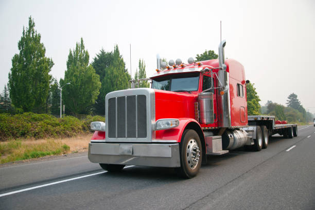 istock Powerful red big rig semi truck with flat bed step down semi trailer move on road for loading cargo 899886196
