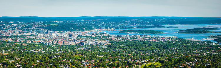 Sweeping aerial panoramic vista across Oslo, Norway's picturesque capital city, from the leafy green suburbs and tranquil housing to the modern downtown developments and historic landmarks looking out over the blue waters of Oslofjorden.