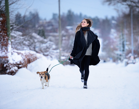 Happy woman running with beagle dog on winter street