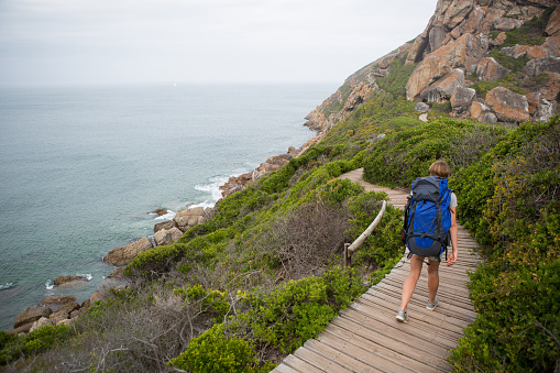 A fit young woman with a backpack on hikes near the coast along a wooden boardwalk.