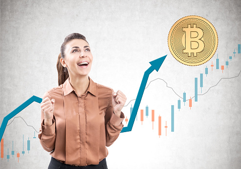Portrait of a young businesswoman wearing a brown blouse and yelling with joy standing against a concrete background with a bitcoin and graphs on it