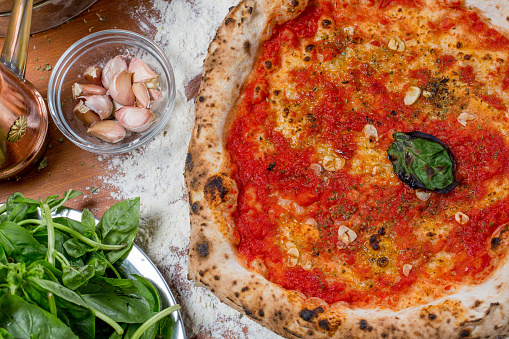 Traditional italian pizza with tomato sauce, garlic, basil and oregano on a wooden table with the ingredients
