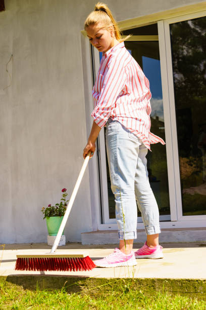 istock Woman using broom to clean up backyard patio 899913932