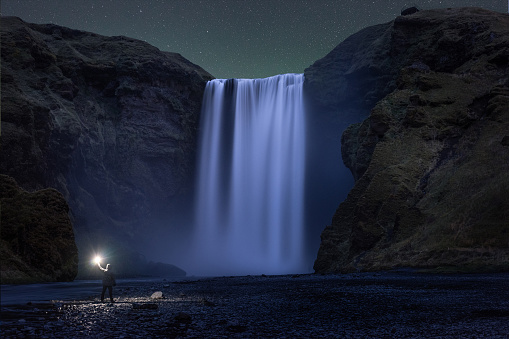 A man lights up his surroundings while looking at the powerful Skogafoss waterfall in South Iceland.