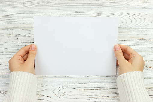 A female hand hold an envelope and post card on the wood desk, top view Copy space.