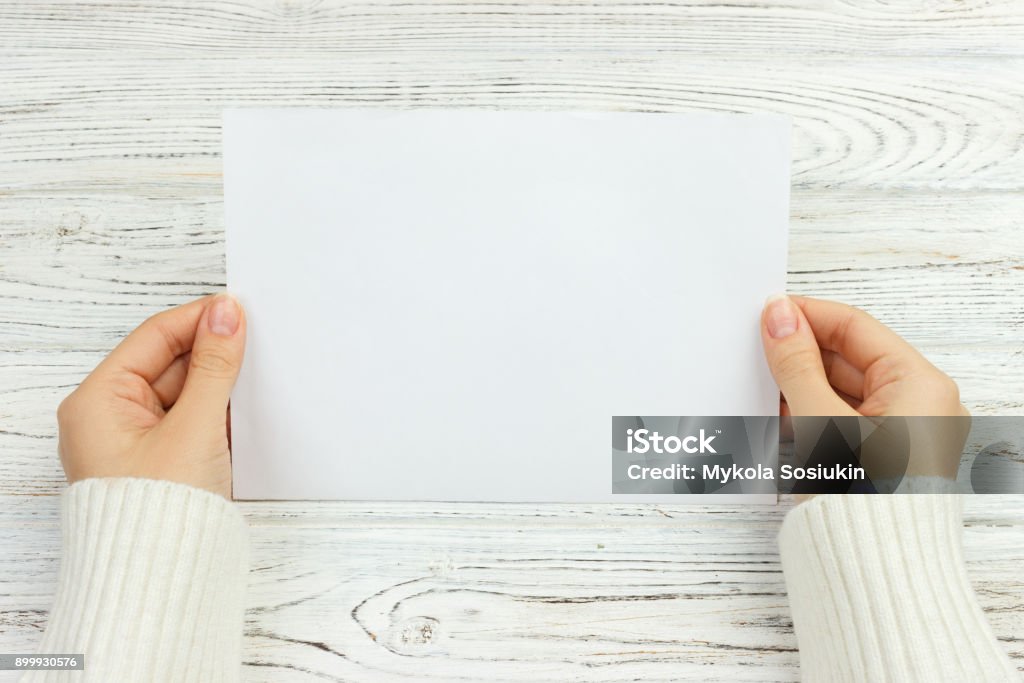 A female hand hold an envelope and post card on the wood desk, top view Copy space A female hand hold an envelope and post card on the wood desk, top view Copy space. Postcard Stock Photo