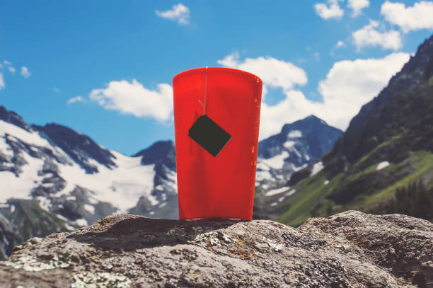 Orange plastic mug with strong tea and tea bag on a snowy winter background.
