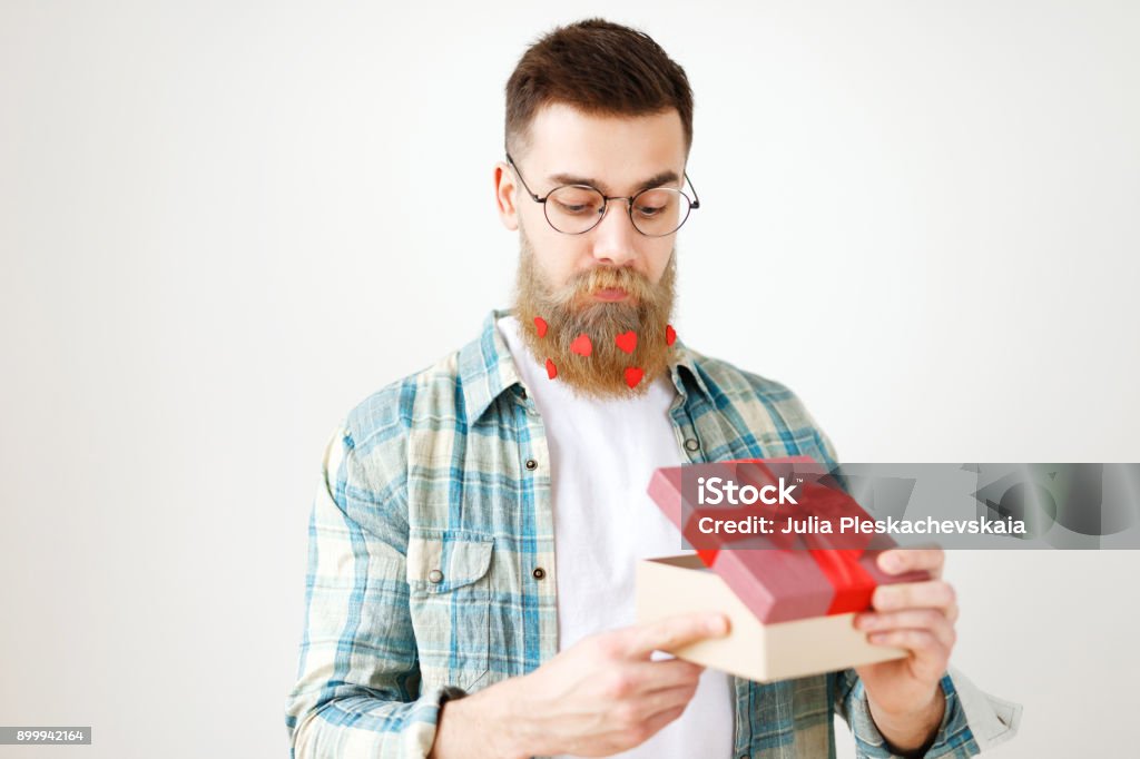 Indoor shot of bearded male model with long thick beard dressed in checkered shirt, opens present box, recieves surprise from girlfriend, isolated over white background. People and celebration Indoor shot of bearded male model with long thick beard dressed in checkered shirt, opens present box, recieves surprise from girlfriend, isolated over white background. People and celebration. Adult Stock Photo