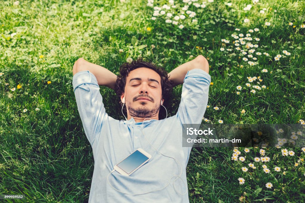 Man napping in the grass Relaxed man lying down at the meadow and listening to music Men Stock Photo