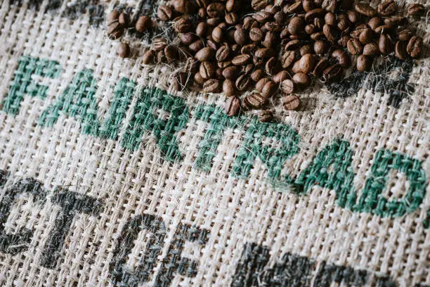 Freshly roasted single origin coffee beans from Mexico lay on a rustic burlap sack.  The words "fair-trade" are printed on the bag, letting the buyer know that it was purchased in fair and sustainable trading conditions.