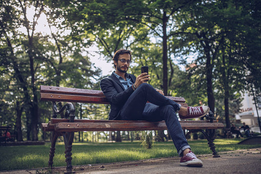 Young businessman sitting in the park and using phone