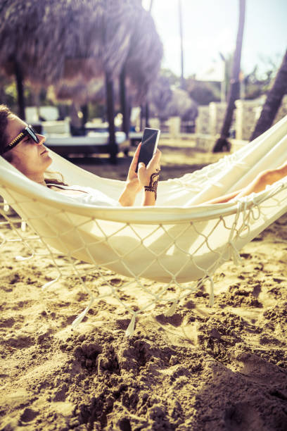 istock Woman surfing the net while relaxing in a hammock by the beach 900005232