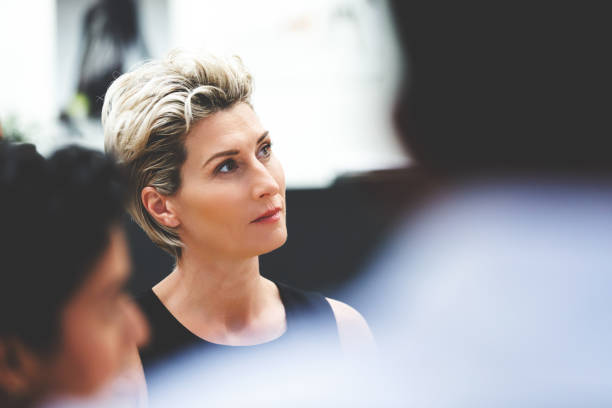 Businesswoman Listening During Meeting Businesswoman Listening During Meeting In Corporate Environment shareholders meeting stock pictures, royalty-free photos & images