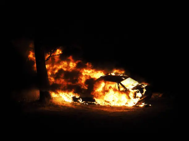 Photo of Burning car. Night. Consequences of the collision with a tree. Car on fire isolated on black background