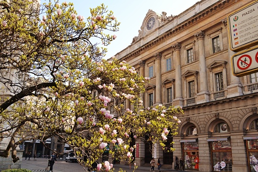 Spring view to the Palace of the Venerable Cathedral Factory in Milan with the ancient artistic decorated clock on a rooftop and magnolia tree flowers.
