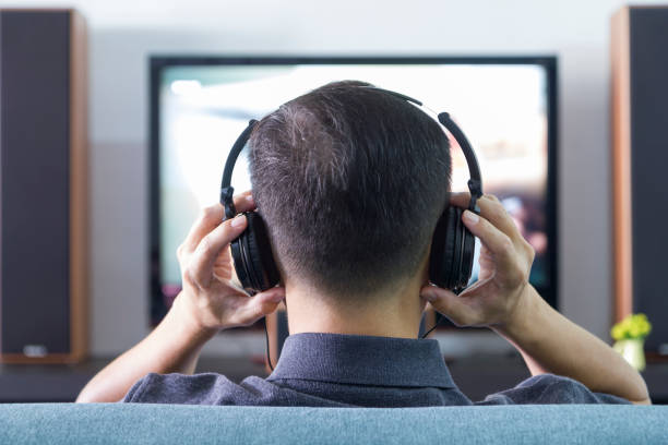 Home Entertainment Back side of an Asian man wearing black heaphones in front of blurry out-of-focus television and home entertainment system background stay tuned concept stock pictures, royalty-free photos & images