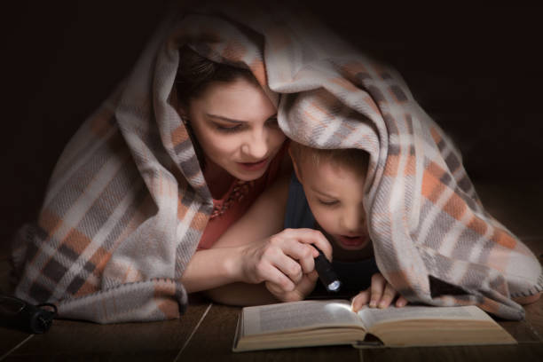 istock Family Mom and little son reading a book with a flashlight under the blanket. 900176842