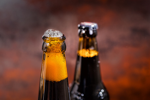 Beer overflow from a just opened beer bottle on dark background. Food and beverages concept