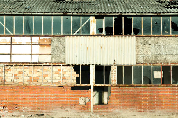 istock Damaged warehouse exterior wall with broken glass windows destroyed in war close up 900200212