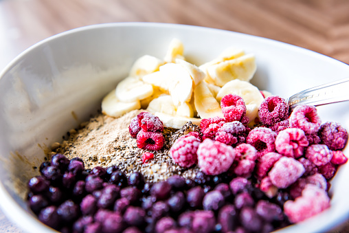 Frozen blueberries, raspberries, banana, maca and chia seeds toppings on oat porridge