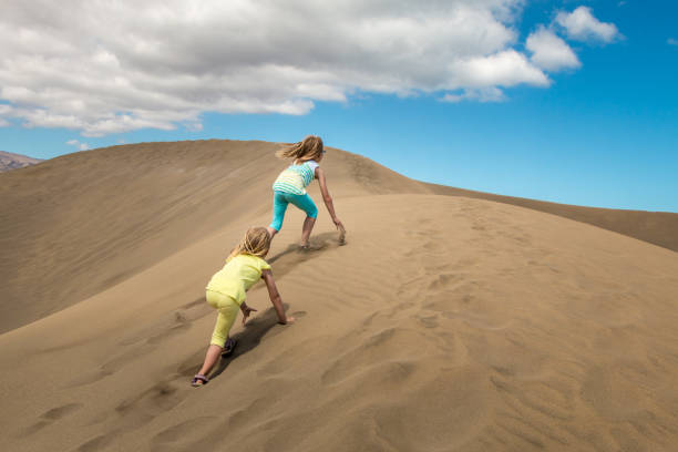 2 children climb a sand dune in the desert