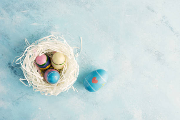 istock Flat lay top view white paper nest with three vintage Easter eggs and one blue egg with red heart on blue background 900212678