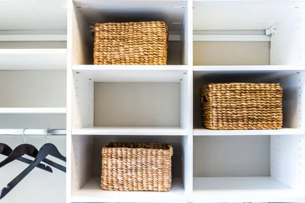 Closeup of woven straw baskets in modern minimalist white closet or laundry room with bright light in staging model house or apartment with hangers