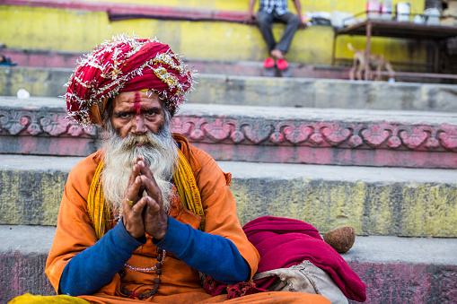Varanasi, Uttar Pradesh, India - March 2023: Portrait of Unidentified sadhu holy male in traditional clothes sitting on ghats near river ganges in varanasi city.