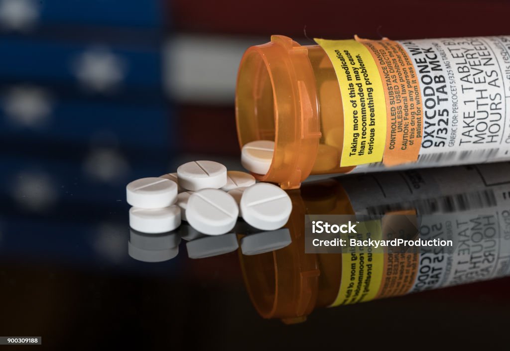 Macro of oxycodone opioid tablets Oxycodone is the generic name for a range of opoid pain killing tablets. Prescription bottle for Oxycodone tablets and pills on wooden table with USA flag in background Oxycodone Stock Photo